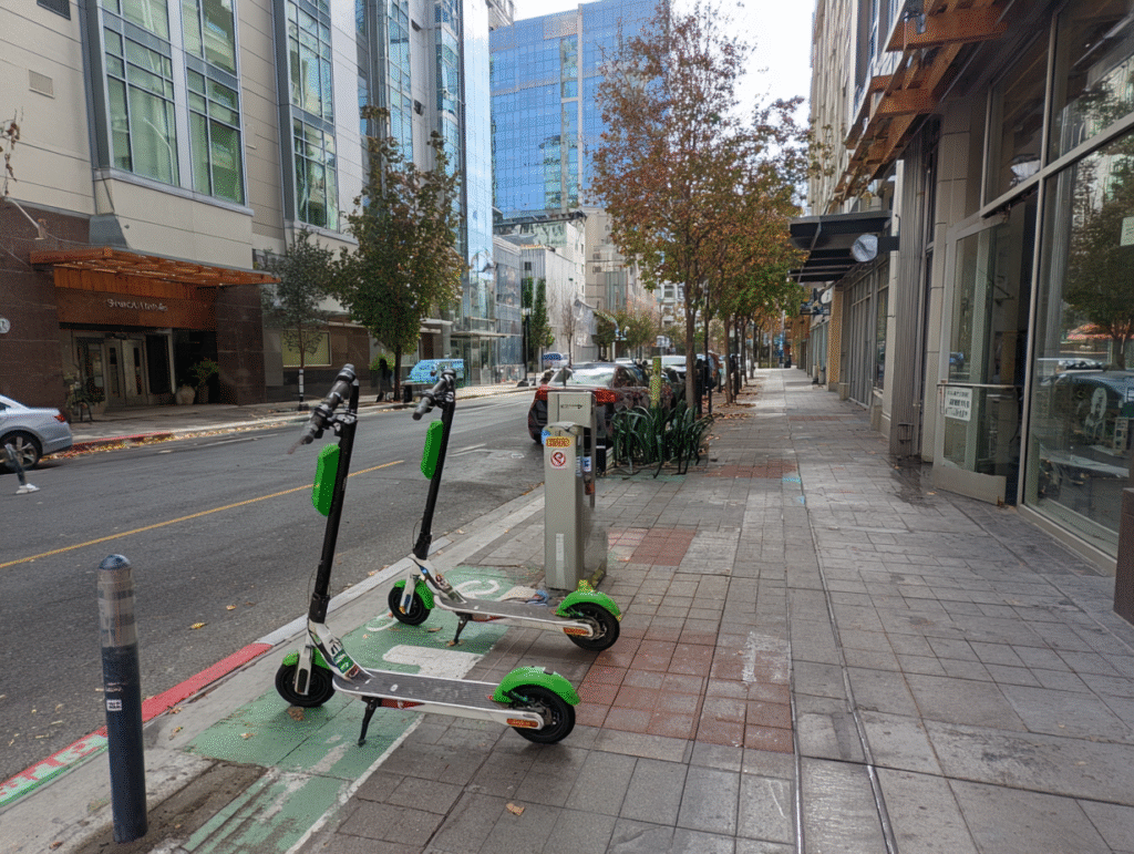 Electric scooters properly parked upright in designated parking zone on city sidewalk without blocking pedestrian access